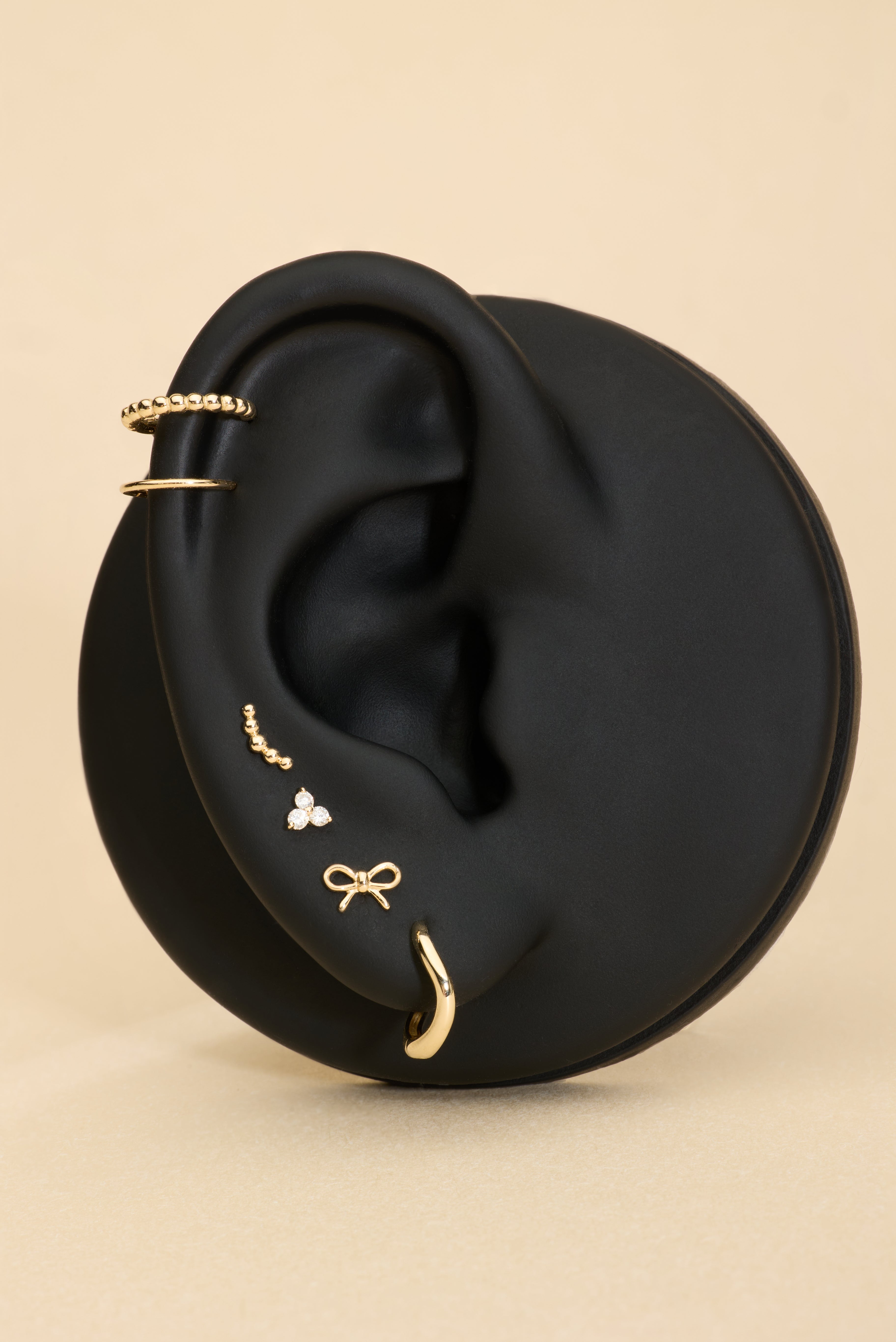 Ear with 14K sold gold stud earrings and solid gold huggie earrings on a beige background