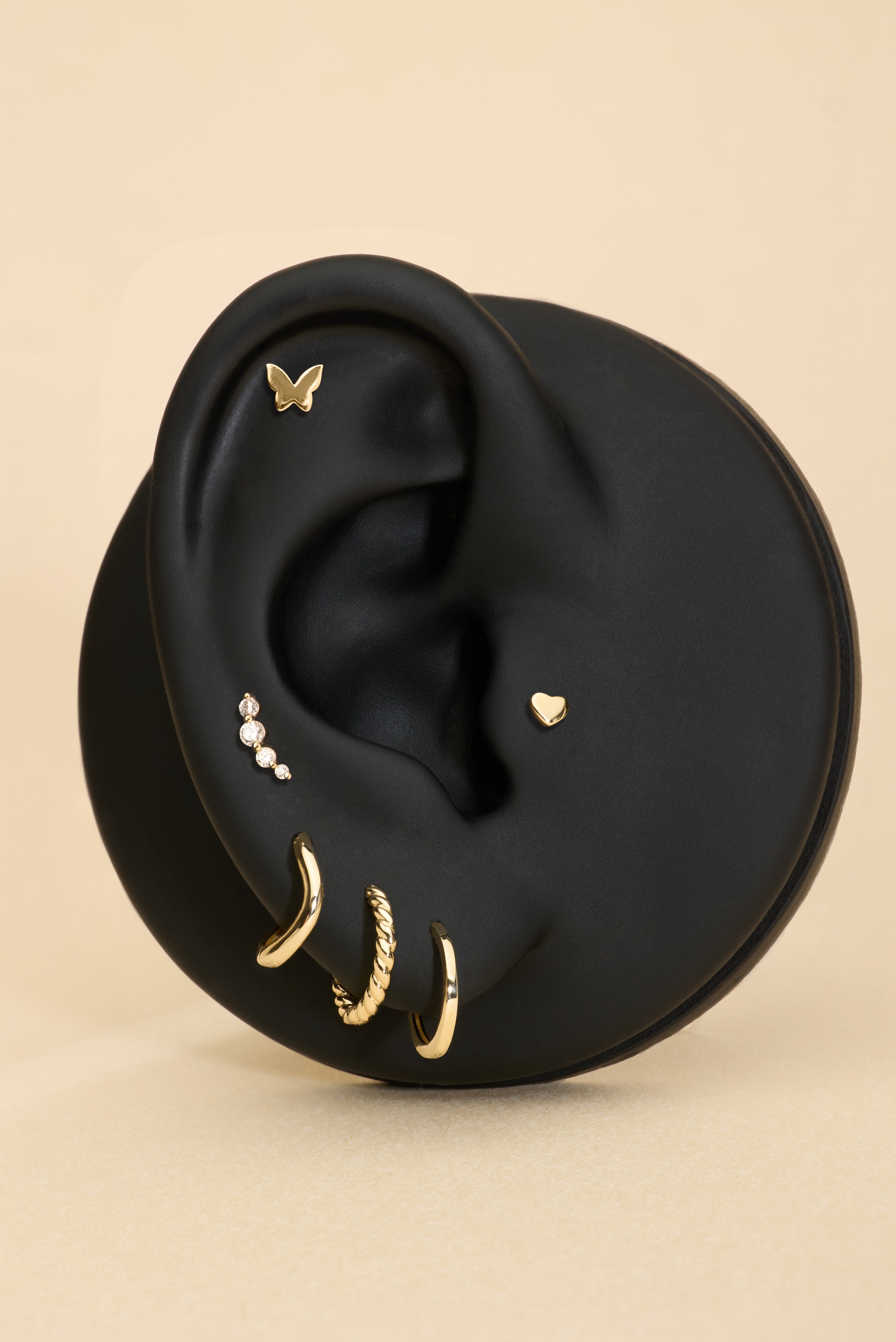 Black ear with gold earrings, butterfly flatback studs, heart flatback and diamond a beige background