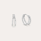 The Mae Twist Double Huggie Earrings in Silver feature a twisted, leafy design. Displayed on a plain background, one earring stands slightly open while the other lies flat, showcasing their intricate detailing.