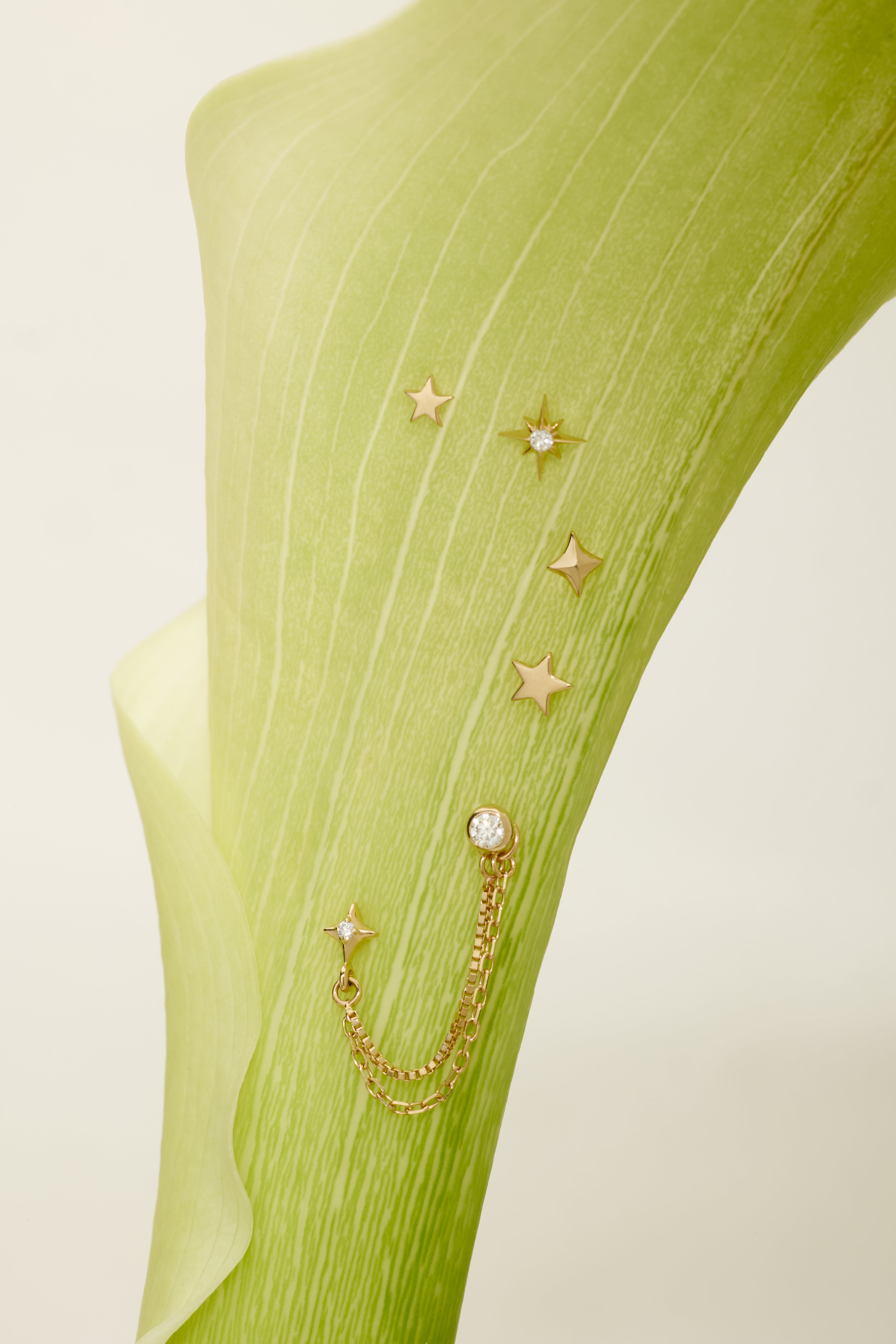 Gold star-shaped earrings with chains on a green fabric background