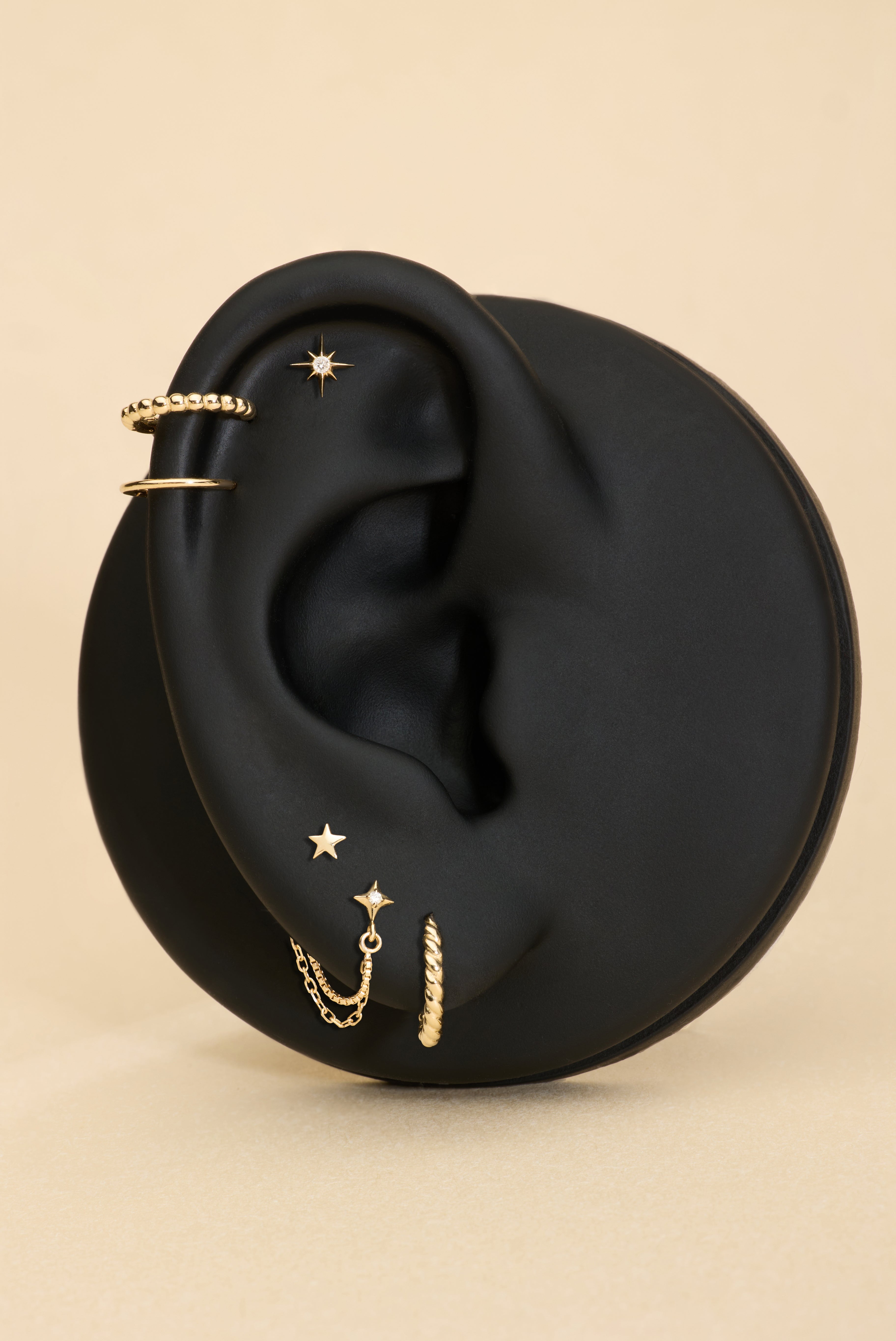 Gold earrings displayed on a black ear with a beige background