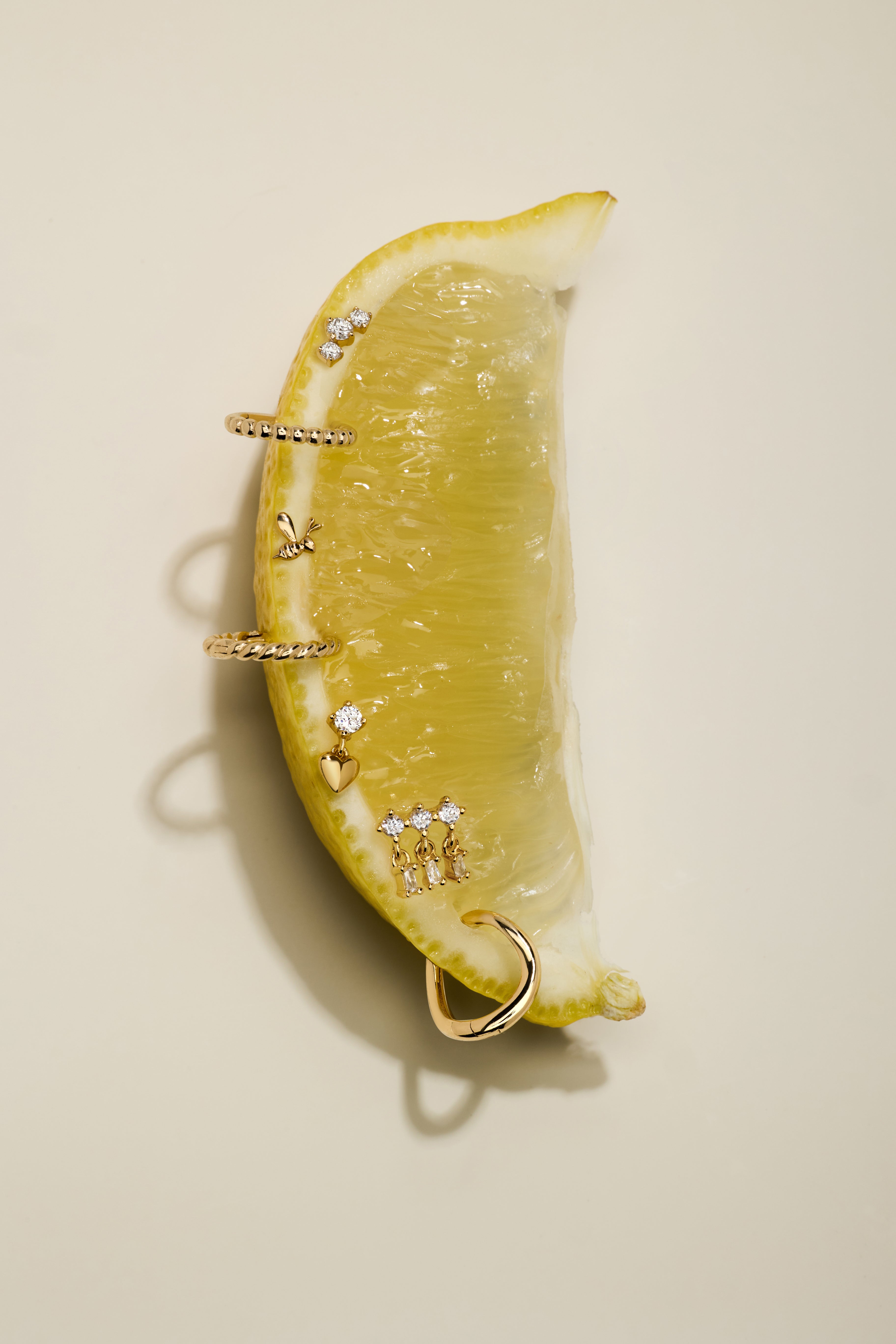 A lemon wedge displays the Lilian Crystal Heart Studs Earrings in Silver, set artfully on its surface and photographed against a neutral beige background.