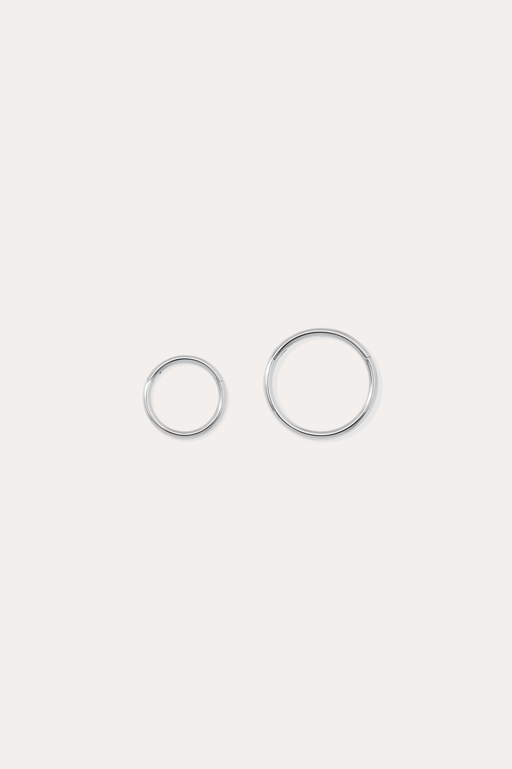 The 14K Solid White Gold 20G Mini Clicker, shown in two shiny sizes on a plain white background, is perfect for use as a clicker or nose ring.