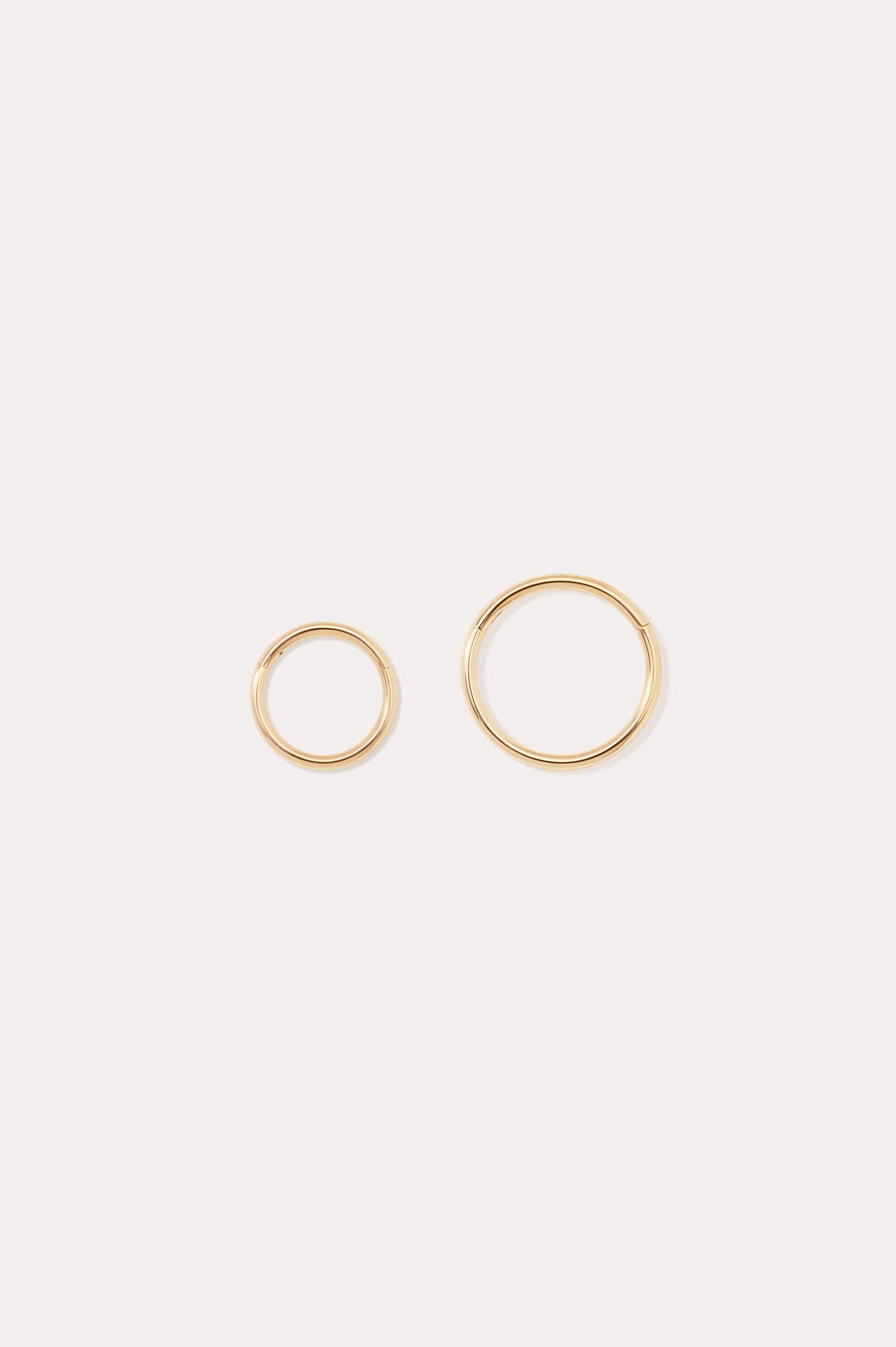 The 14K Solid Yellow Gold 20G Mini Clicker hoops, shown in two sizes on a plain white background, are perfect for classic cartilage wear or as minimalist hoop earrings.
