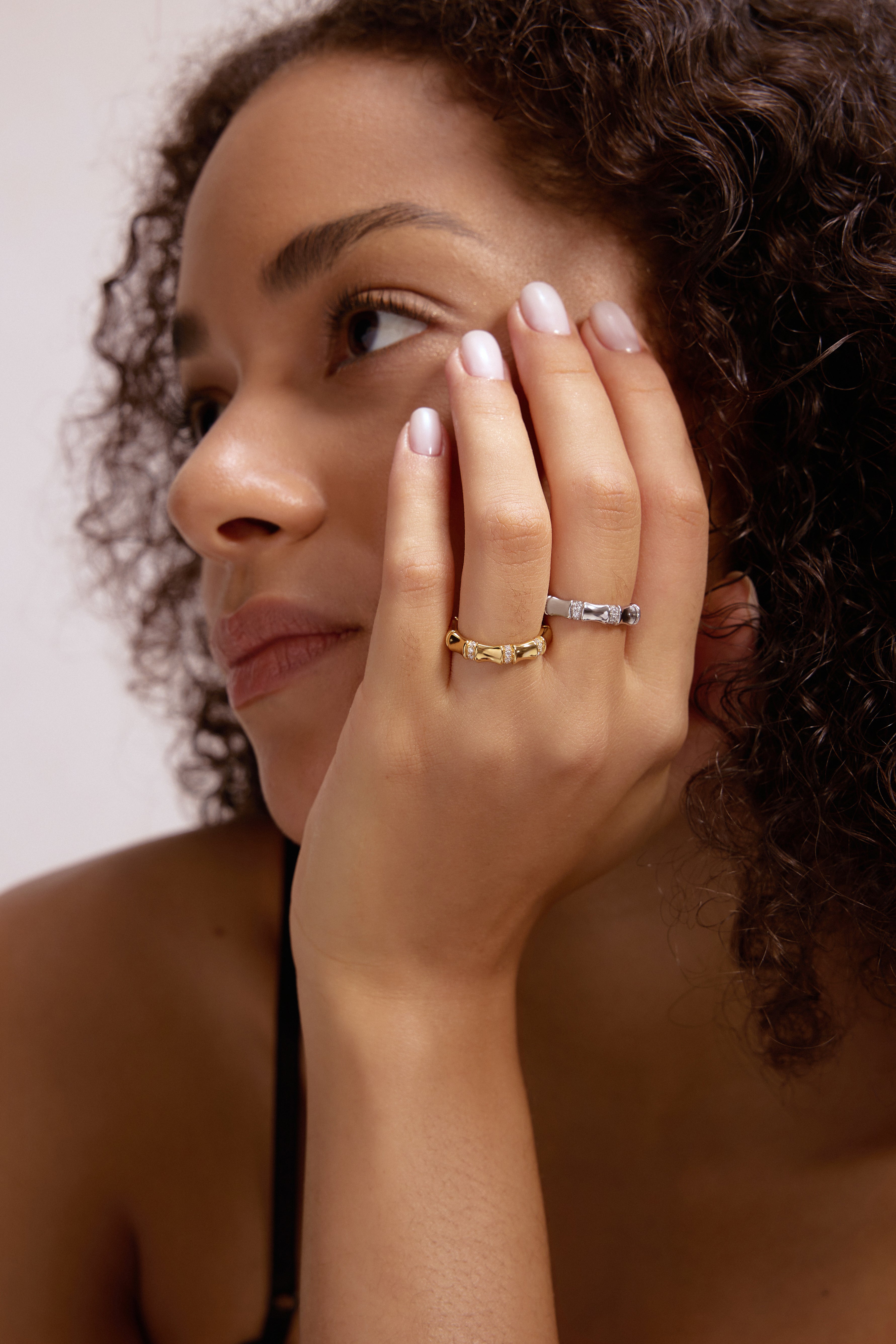 A woman with curly hair rests her chin on her hand, displaying the Bamboo Chunky Crystal Ring in Silver. She looks thoughtfully into the distance, and her neatly manicured nails complement the recycled sterling silver ring.