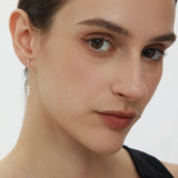 A close-up of a woman with fair skin and brown hair pulled back, wearing a black top and the Eden Trio Pearl Drop Earrings in Silver, looking slightly to the side with a neutral expression.