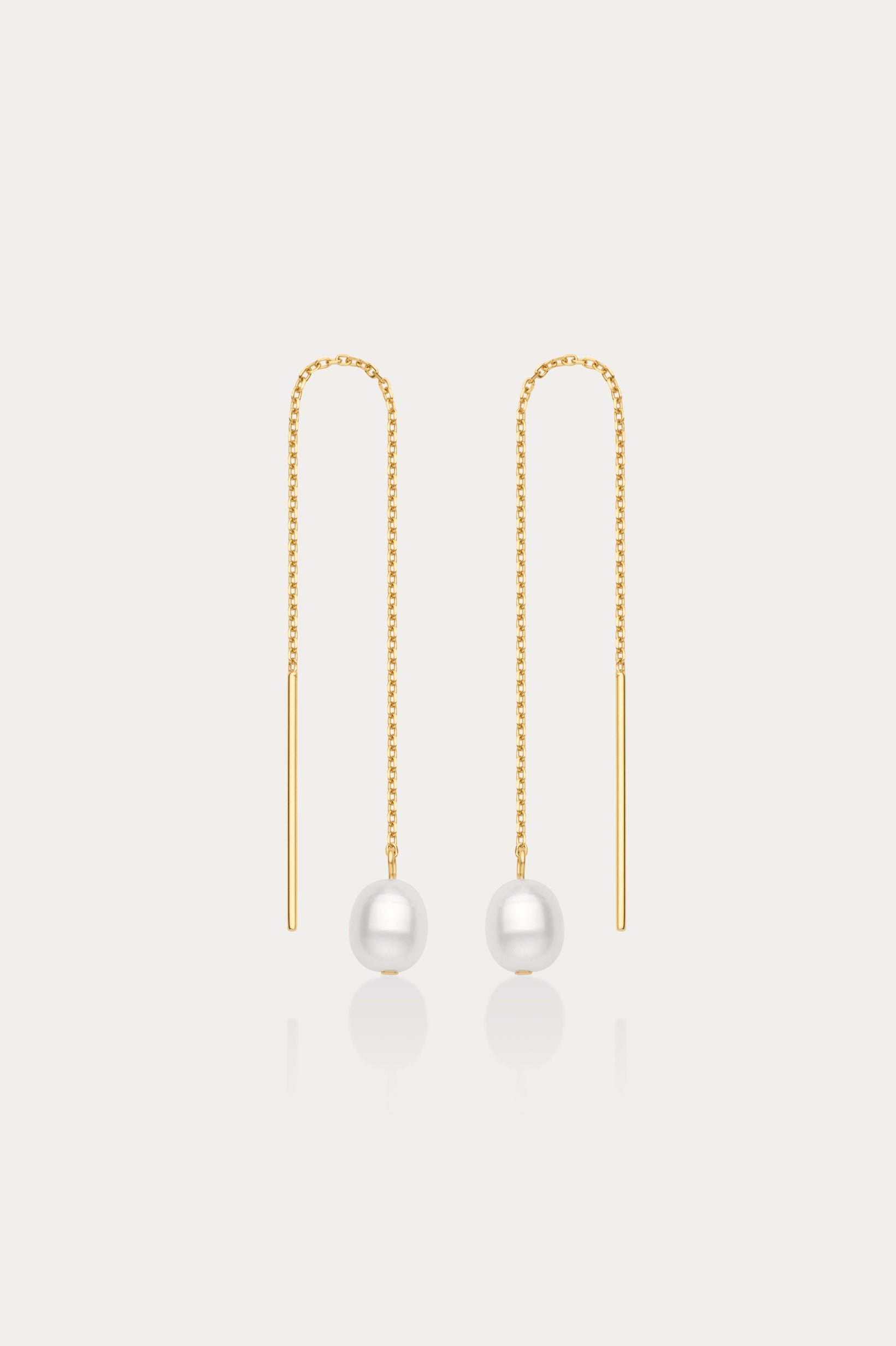 The Eira Pearl Drop Threader Earrings in Gold feature delicate chains ending with a single round white pearl, offering a minimalist and elegant look against a plain white background.