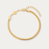 The Estelle Herringbone Chain Bracelet in Gold is a 3mm bracelet with an adjustable clasp, extension chain, and a small flat charm, perfect for bracelet stacking and shown on a light background.