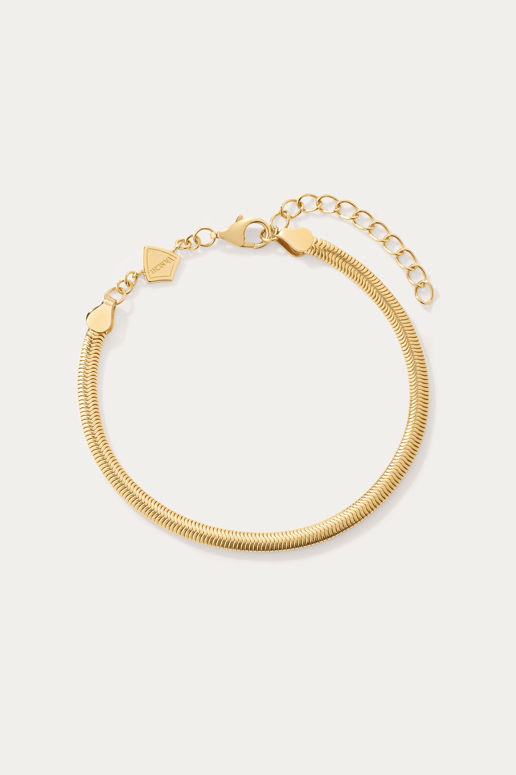 The Estelle Herringbone Chain Bracelet in Gold is a 3mm bracelet with an adjustable clasp, extension chain, and a small flat charm, perfect for bracelet stacking and shown on a light background.