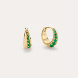 The Georgie Crystal Knife Edge Huggie Hoop Earrings in Green feature small gold hoops with a row of green crystals along the front, shown against a plain light background.