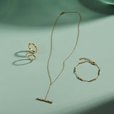 A delicate gold jewelry set arranged on a mint green surface, featuring a ring, bracelet, and the Bamboo Chain Y-Bar Lariat Necklace in Gold, each piece casting soft shadows.