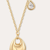 The Nora Double Pendant Necklace in Gold features a sculptural pendant paired with a small, teardrop-shaped cubic zirconia charm suspended just above it.
