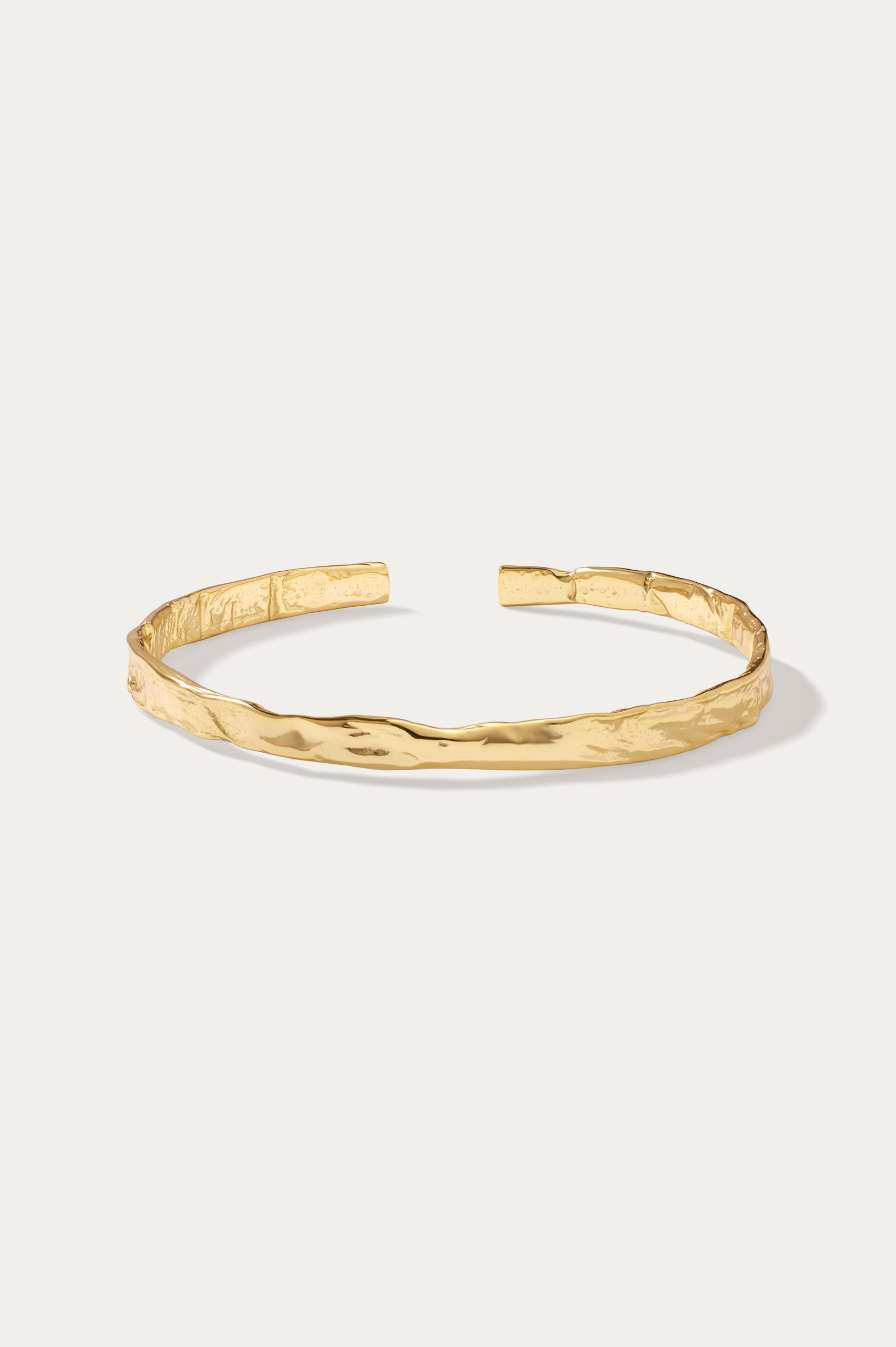 The Elodie Textured Torque Bangle in Gold is a sleek, open bracelet with a polished finish and lava-inspired texture, shown on a plain white background.