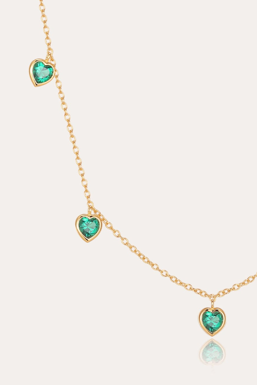 The Thea Green Heart Pendant Gold Necklace is a delicate adjustable gold chain adorned with five evenly spaced, small green cubic zirconia heart-shaped gemstones.