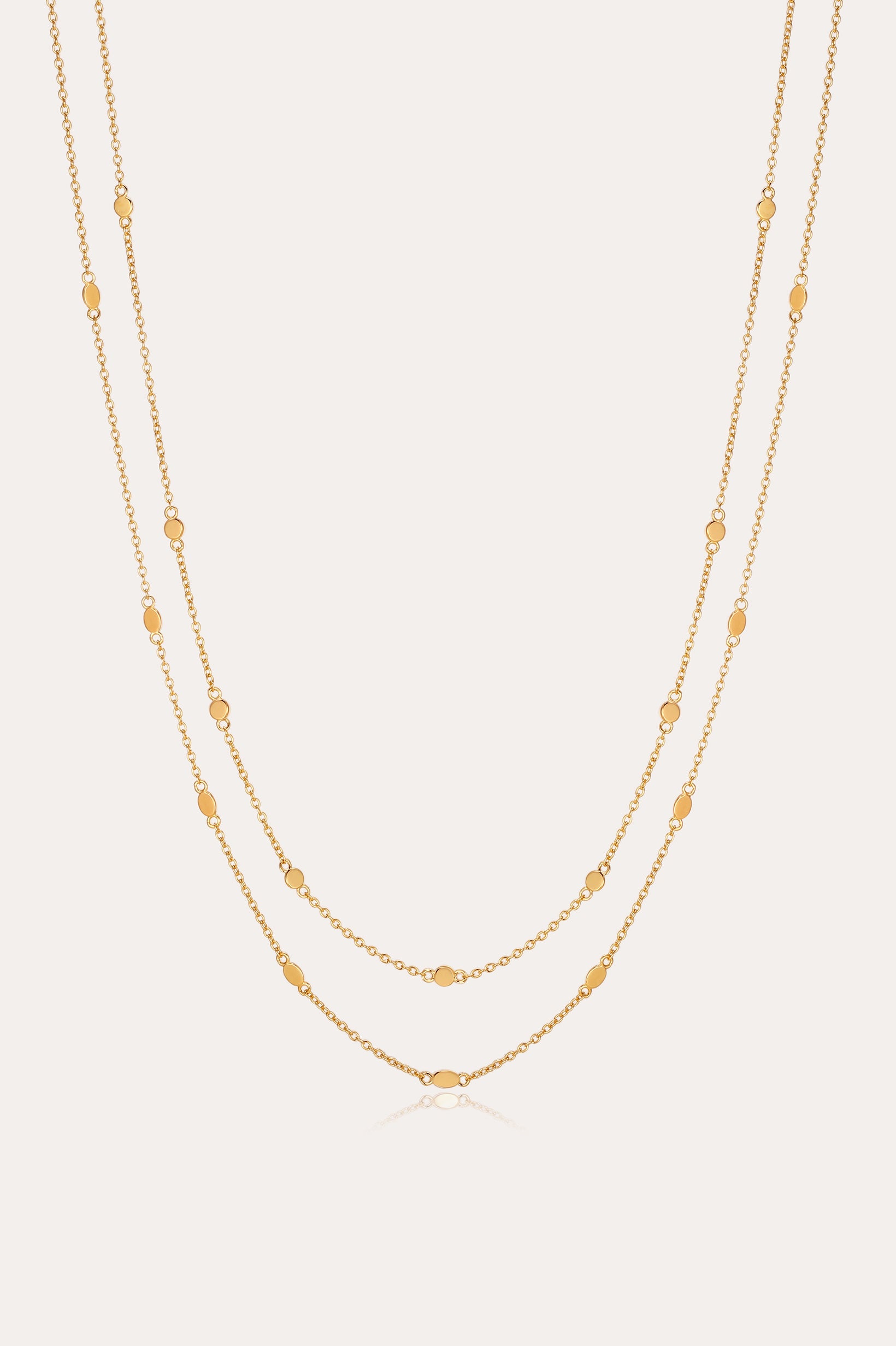 The Simona Double Chain Stacking Necklace in Gold features two delicate chains with evenly spaced oval and round bead accents, making it a minimalist piece thats perfect for layering or wearing solo against a light background.