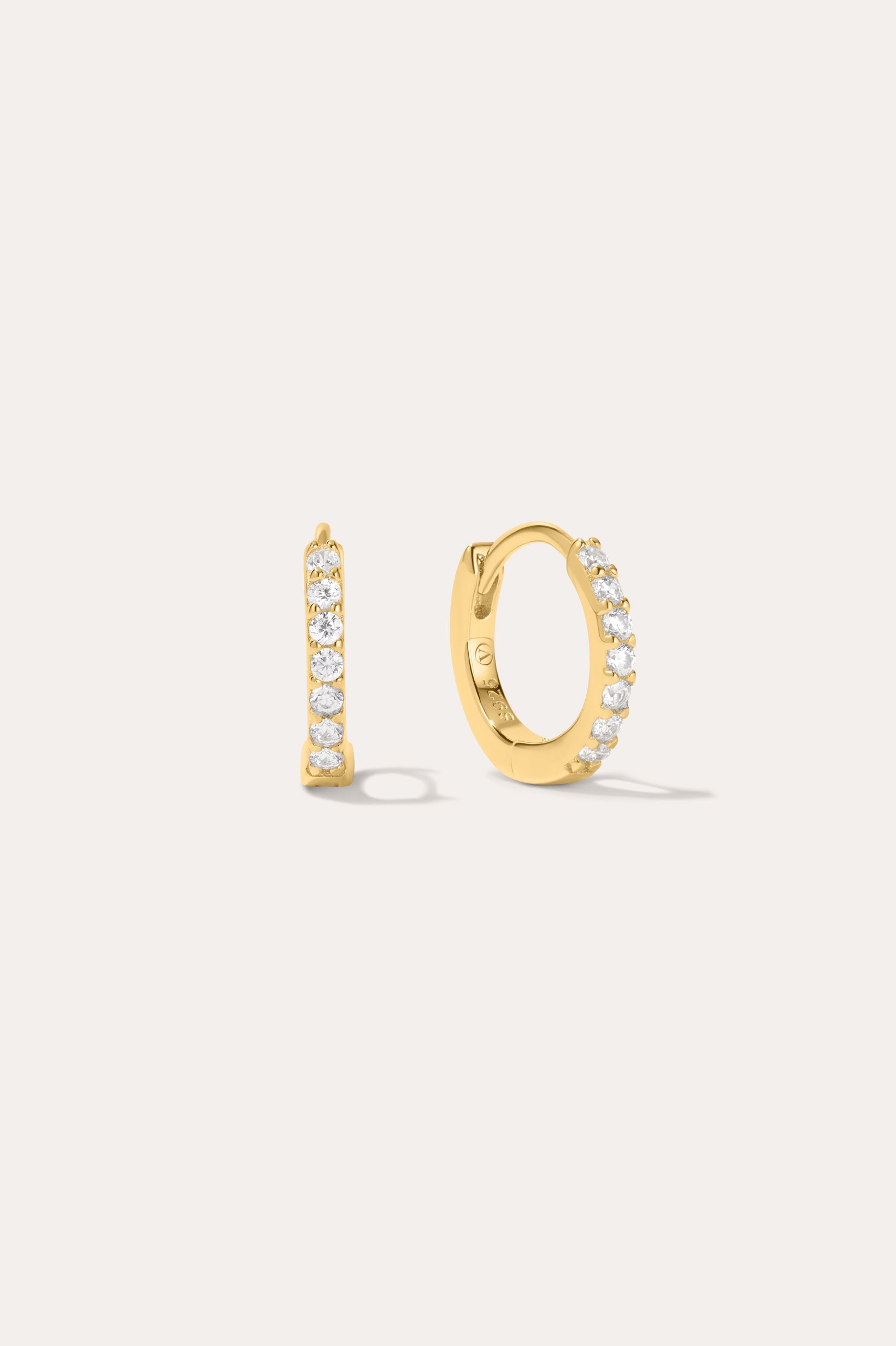 The Kiki Crystal Huggie Earrings in Gold feature a row of clear round crystals on 18k gold-plated hoops. One earring is shown from the side, the other from the front, against a light background—ideal for stacking.