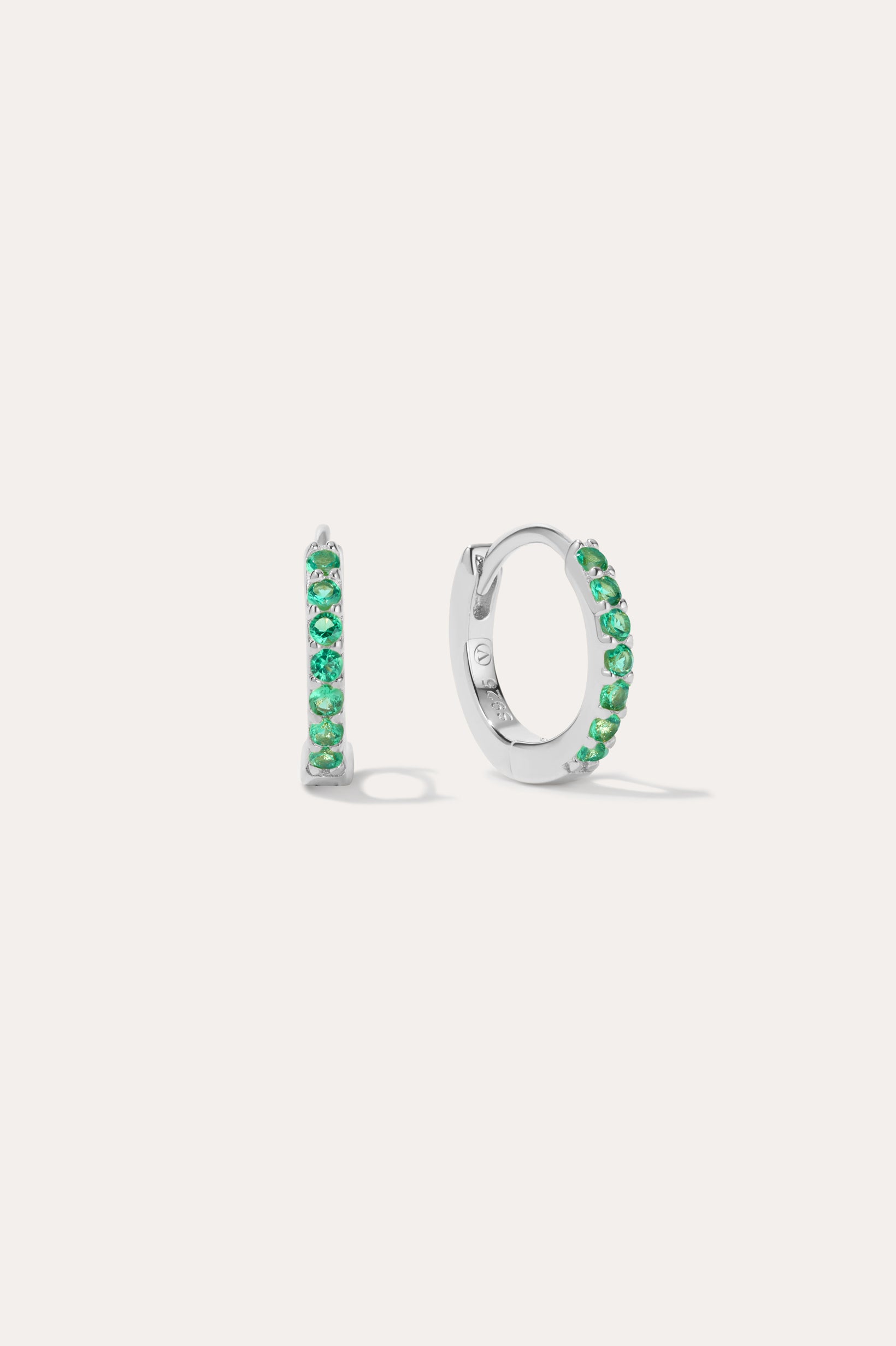 The Kiki Crystal Huggie Earrings in Sterling Silver/Green are displayed on a white background, with one earring facing forward and the other shown from the side.