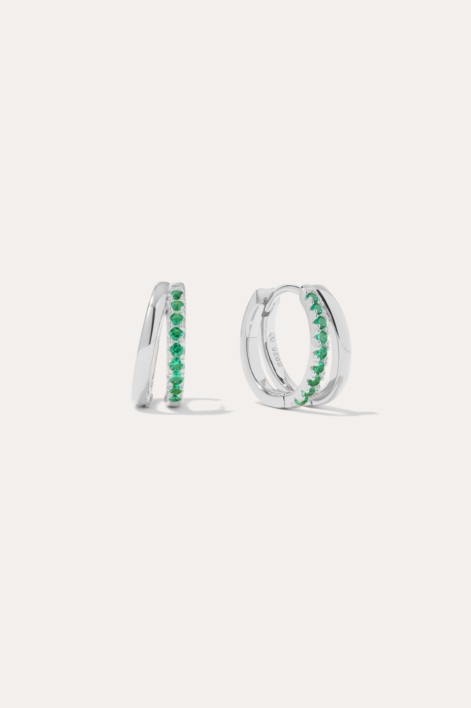The Kira Crystal Double Hoop Huggies in Sterling Silver/Green feature a row of green gemstones along the front and are displayed against a plain white background.