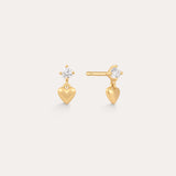 The Lilian Crystal Heart Studs Earrings in Gold feature a small gold heart charm dangling below a sparkling round crystal, displayed on a plain light background.