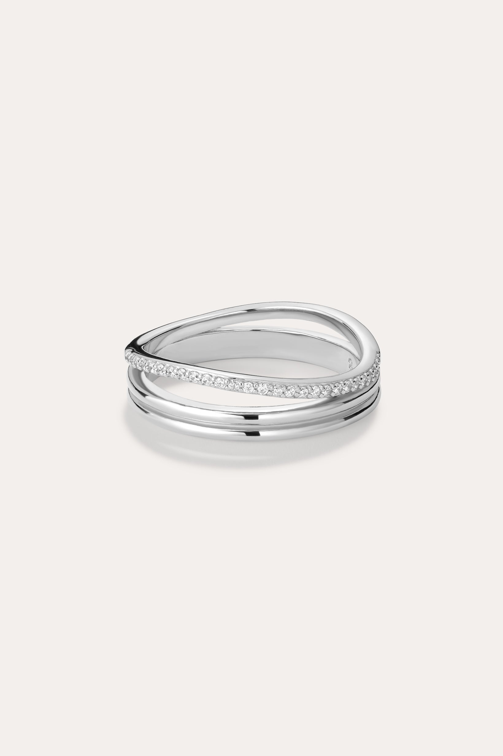 The Noor Pavé Triple Band Ring in Silver showcases a modern overlapping design with a polished finish and a row of sparkling pavé diamonds along one edge, elegantly set against a light background.