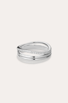 The Noor Pavé Triple Band Ring in Silver showcases a modern overlapping design with a polished finish and a row of sparkling pavé diamonds along one edge, elegantly set against a light background.