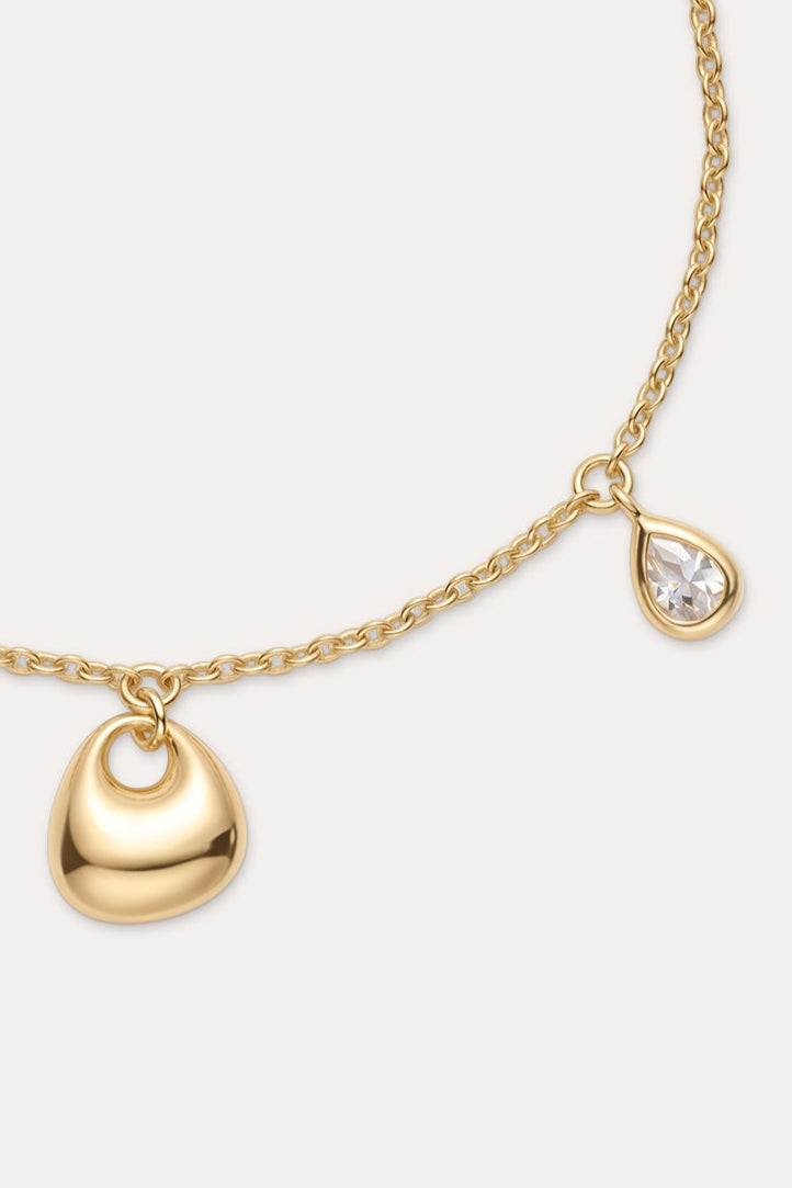 The Nora Double Pendant Bracelet in Gold features a small gold heart charm and a teardrop-shaped cubic zirconia, finished with an adjustable clasp and extension chain.