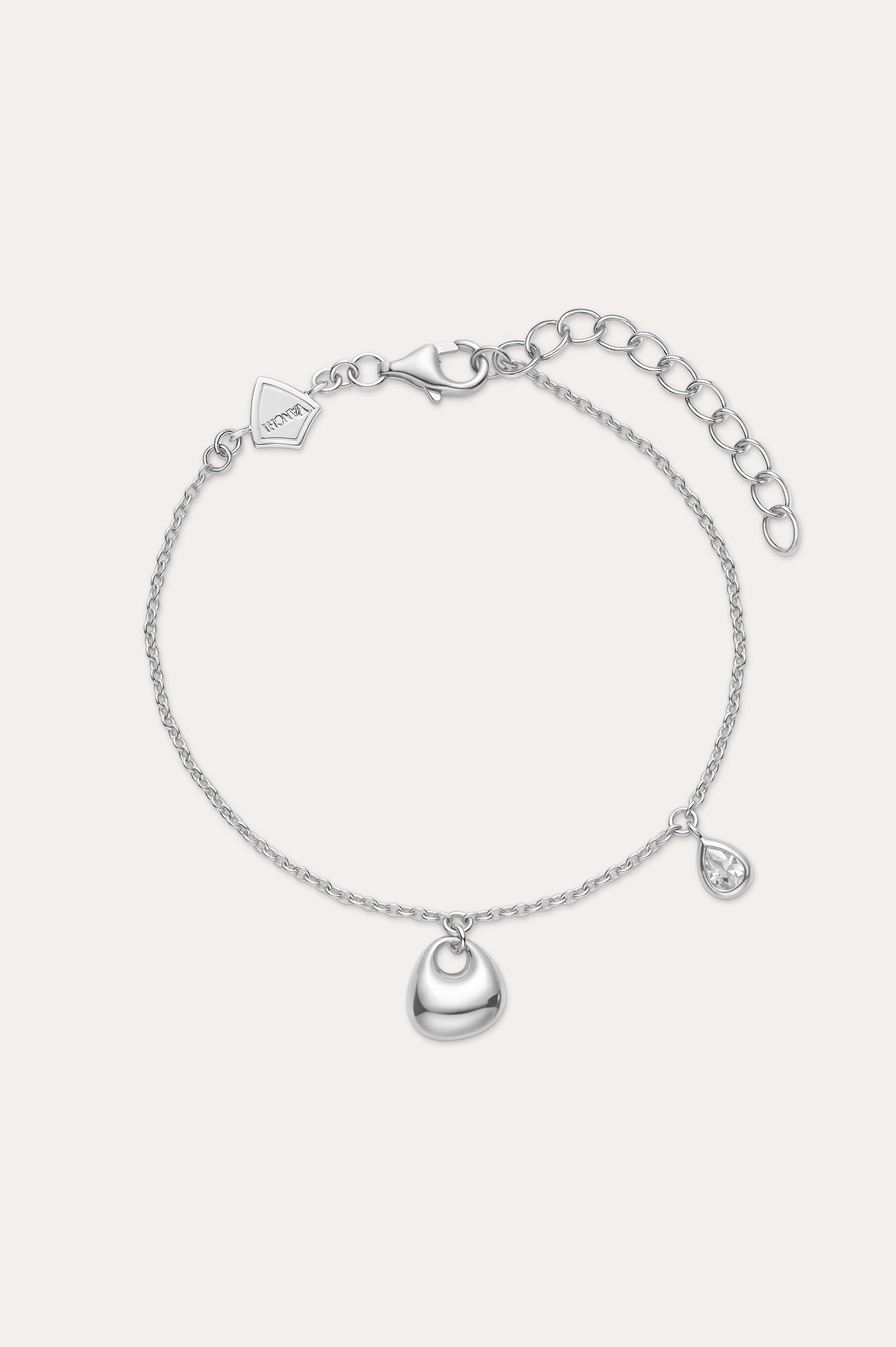 The Nora Double Pendant Bracelet in Silver features a polished heart charm at the center and a small teardrop pendant, both accented with cubic zirconia, plus an adjustable clasp and logo tag near the fastening.