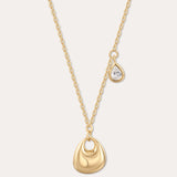 The Nora Double Pendant Necklace in Gold features a smooth sculptural pendant and a delicate teardrop charm with clear cubic zirconia, displayed on a plain light background.