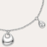 The Nora Double Pendant Bracelet in Silver features an adjustable clasp, a small heart-shaped charm, and a tiny cubic zirconia teardrop charm dangling side by side.