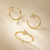 Three Reneé Triangle Linear Hoop Stud Earrings in Gold, each adorned with a diamond-studded triangle, are artfully arranged on a beige background with soft shadows.