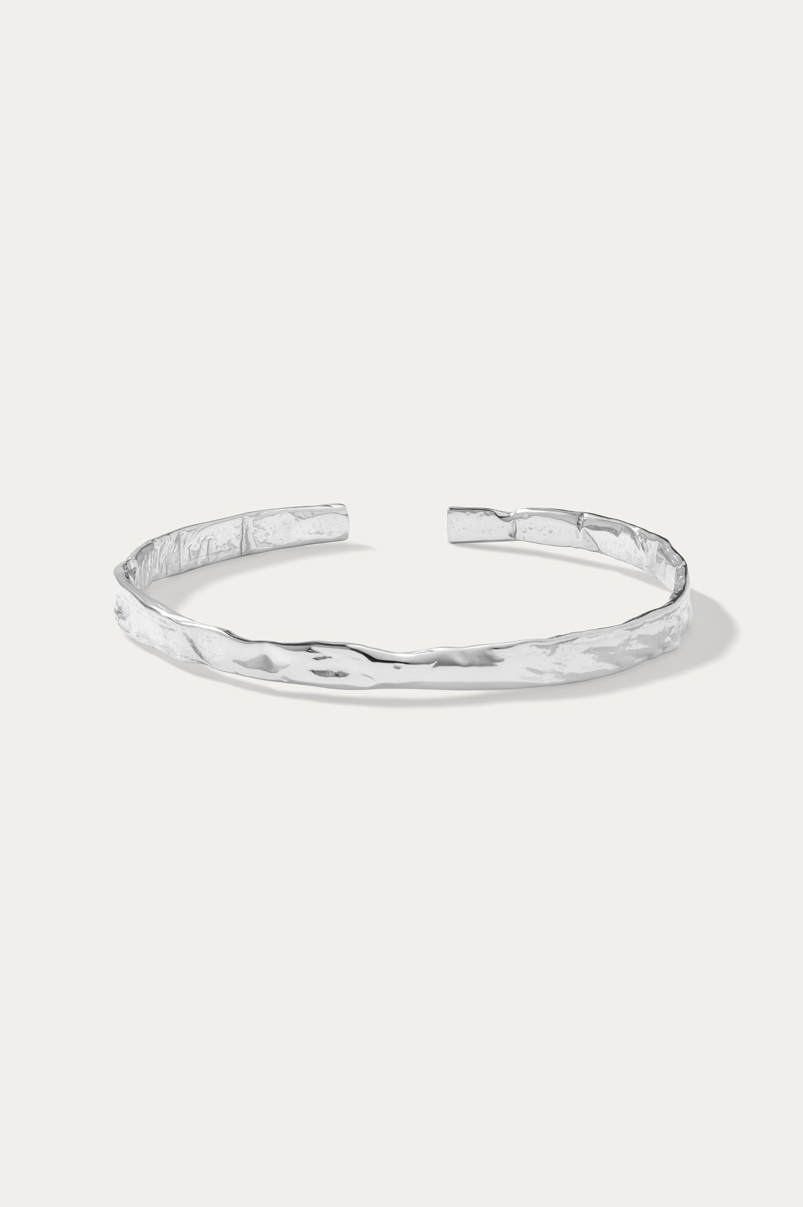 The Elodie Textured Torque Bangle in Silver is a minimalist, open-ended bracelet with a hammered finish, showcased on a plain white background.
