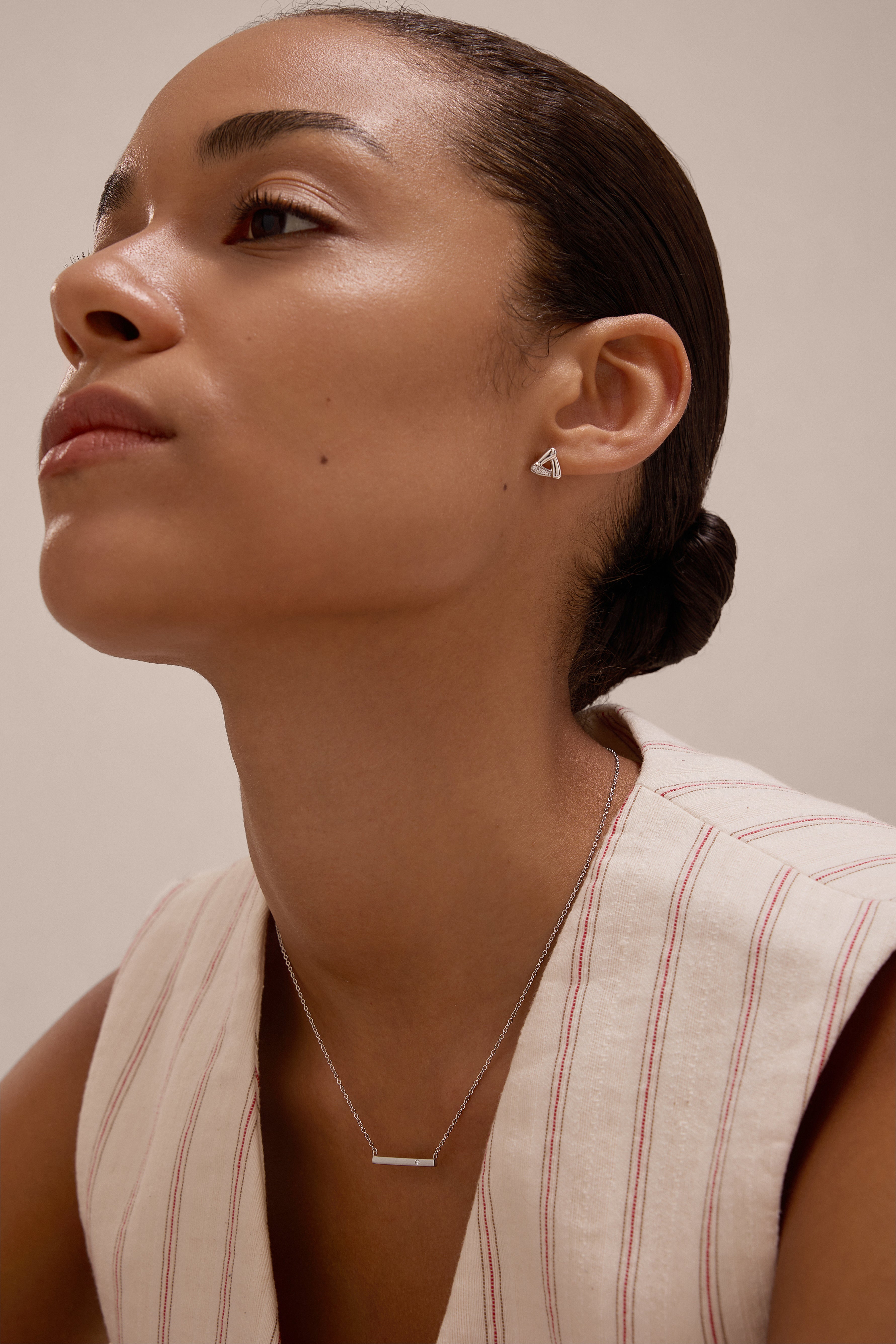 A woman with slicked-back hair wears a sleeveless, cream top with red stripes and the Colette Droop Link Studs in Silver, paired with a simple bar necklace. She gazes slightly upward against a neutral background.