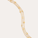 A triple layered gold bracelet with chain links and small circular embellishments, fastened with a lobster clasp.