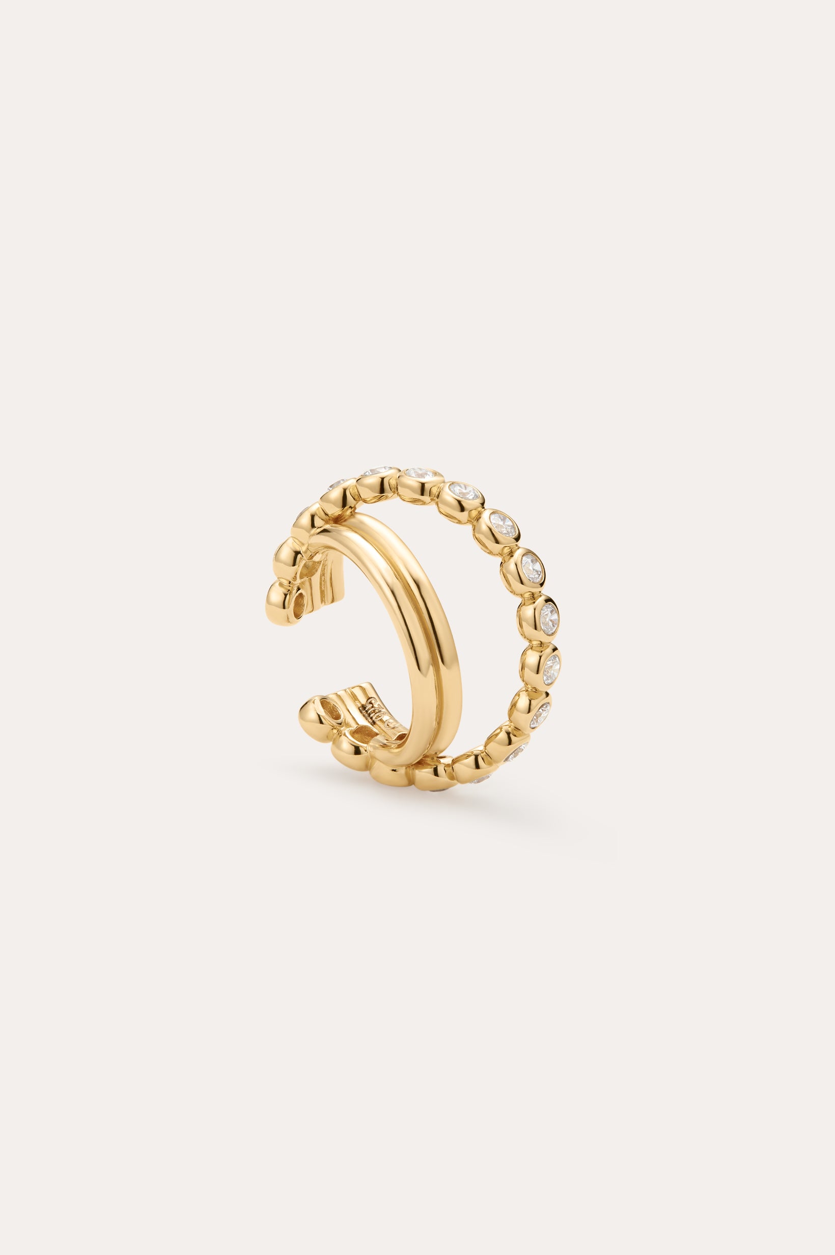 The Vina Crystal Bezel Ear Cuff in Gold features a beaded design with small, round clear cubic zirconia along the outer edge, shown on a light beige background.