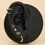 Ear with 14K sold gold stud earrings and solid gold huggie earrings on a beige background