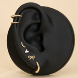 Ear with 14K sold gold stud earrings and solid gold huggie earrings on a beige background