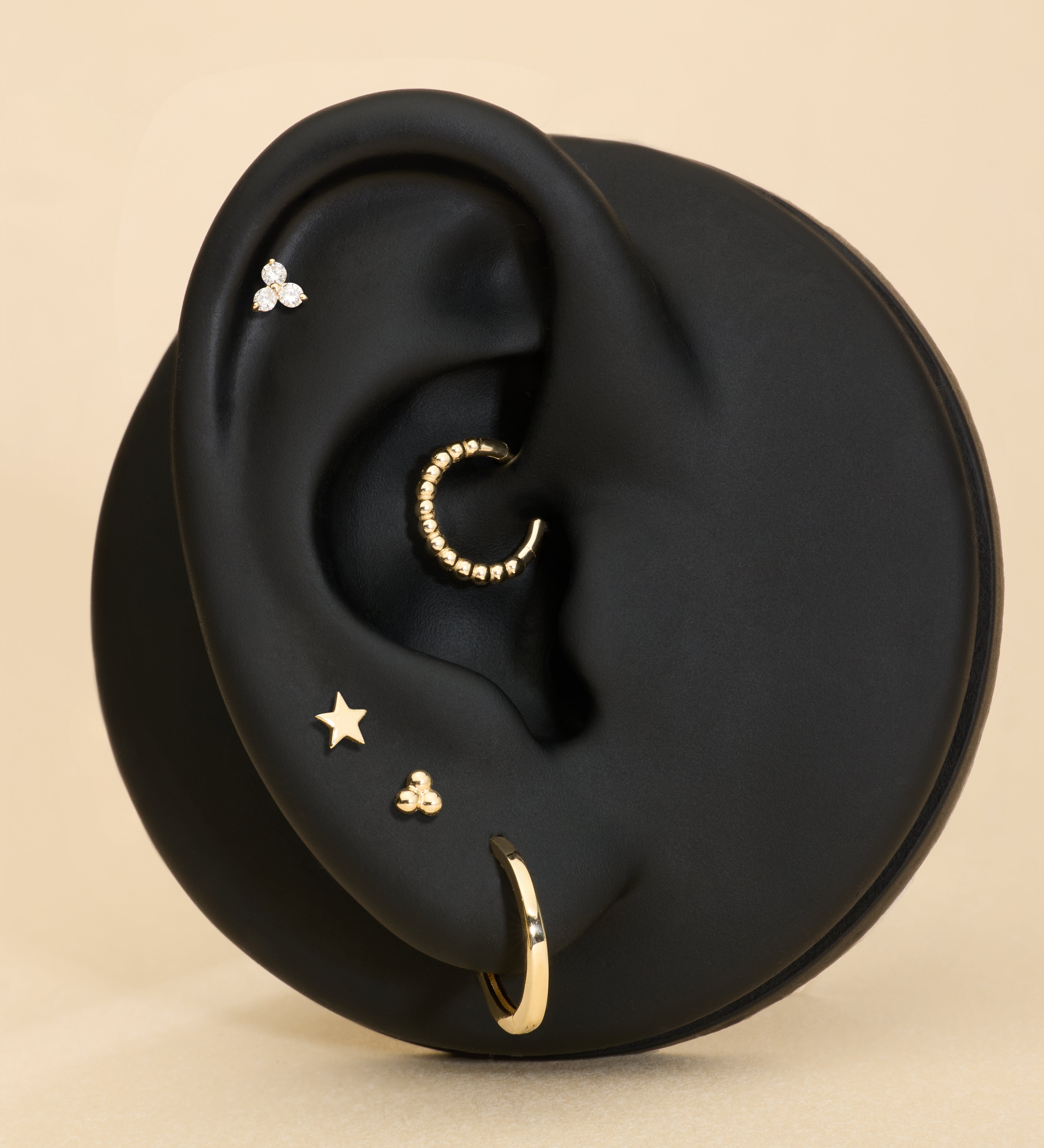 Ear with gold earrings on a beige background