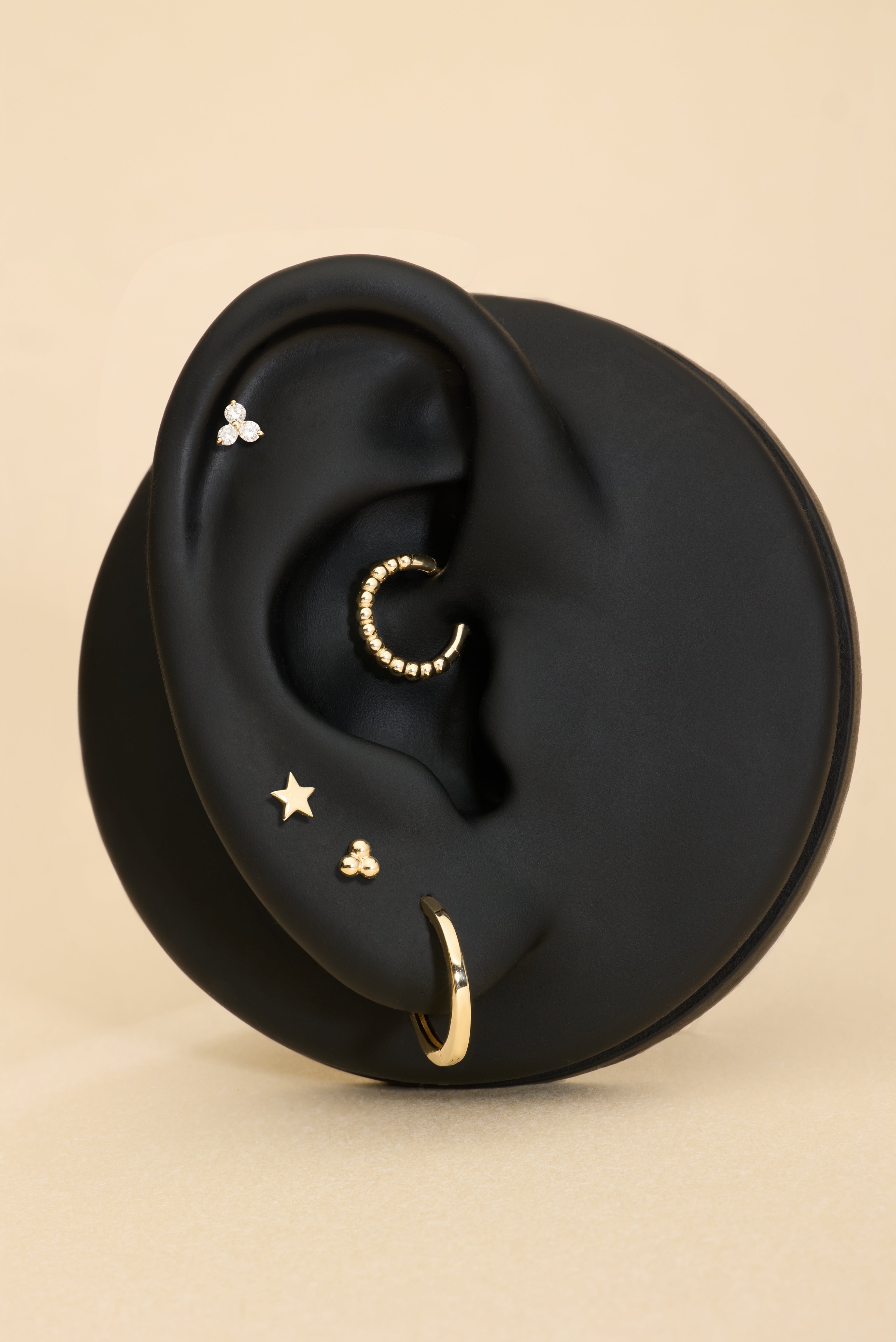Ear with gold earrings on a beige background