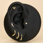 Black ear with gold earrings, butterfly flatback studs, heart flatback and diamond a beige background
