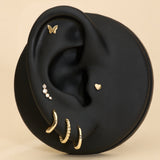 Black ear with gold earrings, butterfly flatback studs, heart flatback and diamond a beige background