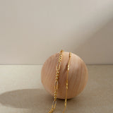 The Bamboo Chain Bracelet in Gold, featuring a delicate 18k gold-plated design, is elegantly displayed draped over a smooth, light wooden sphere against a neutral beige background with soft lighting and gentle shadows.