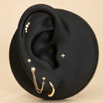 A black ear-shaped display showcases the 14K Solid Yellow Gold Four Point Star Flat Back Stud with other jewelry pieces against a beige background.
