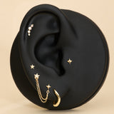 A black ear-shaped display showcases the 14K Solid Yellow Gold Four Point Star Flat Back Stud with other jewelry pieces against a beige background.