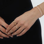 A person with neat nails wears the Reneé Minimalist Triangle Ring in Gold and a delicate gold bracelet, all set against a black outfit background.