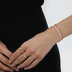 A person in a black dress displays manicured nails and wears two gold bracelets plus the Reneé Minimalist Triangle Ring in Gold, each piece featuring a modern triangle design.