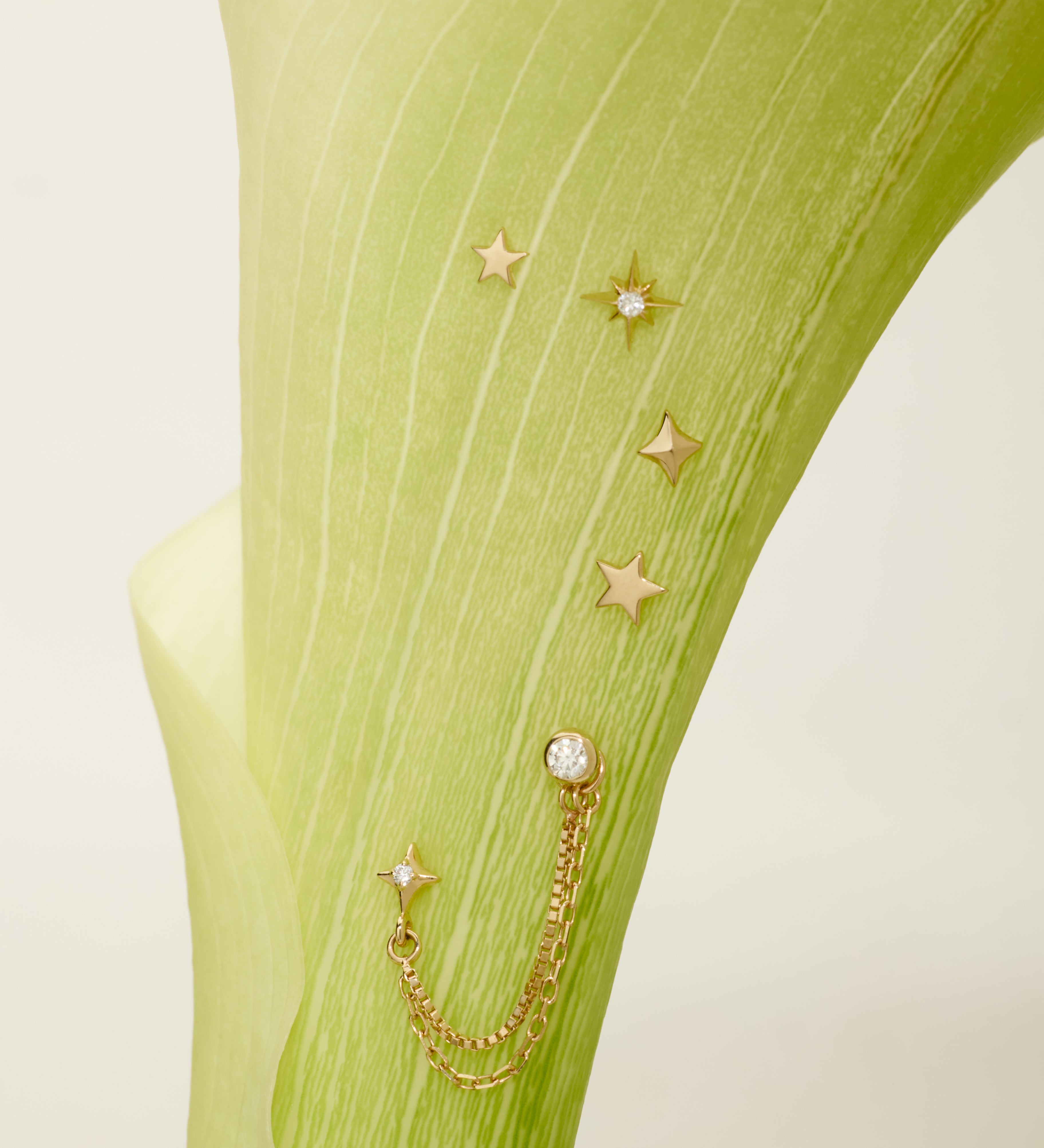 Gold star-shaped earrings with chains on a green fabric background