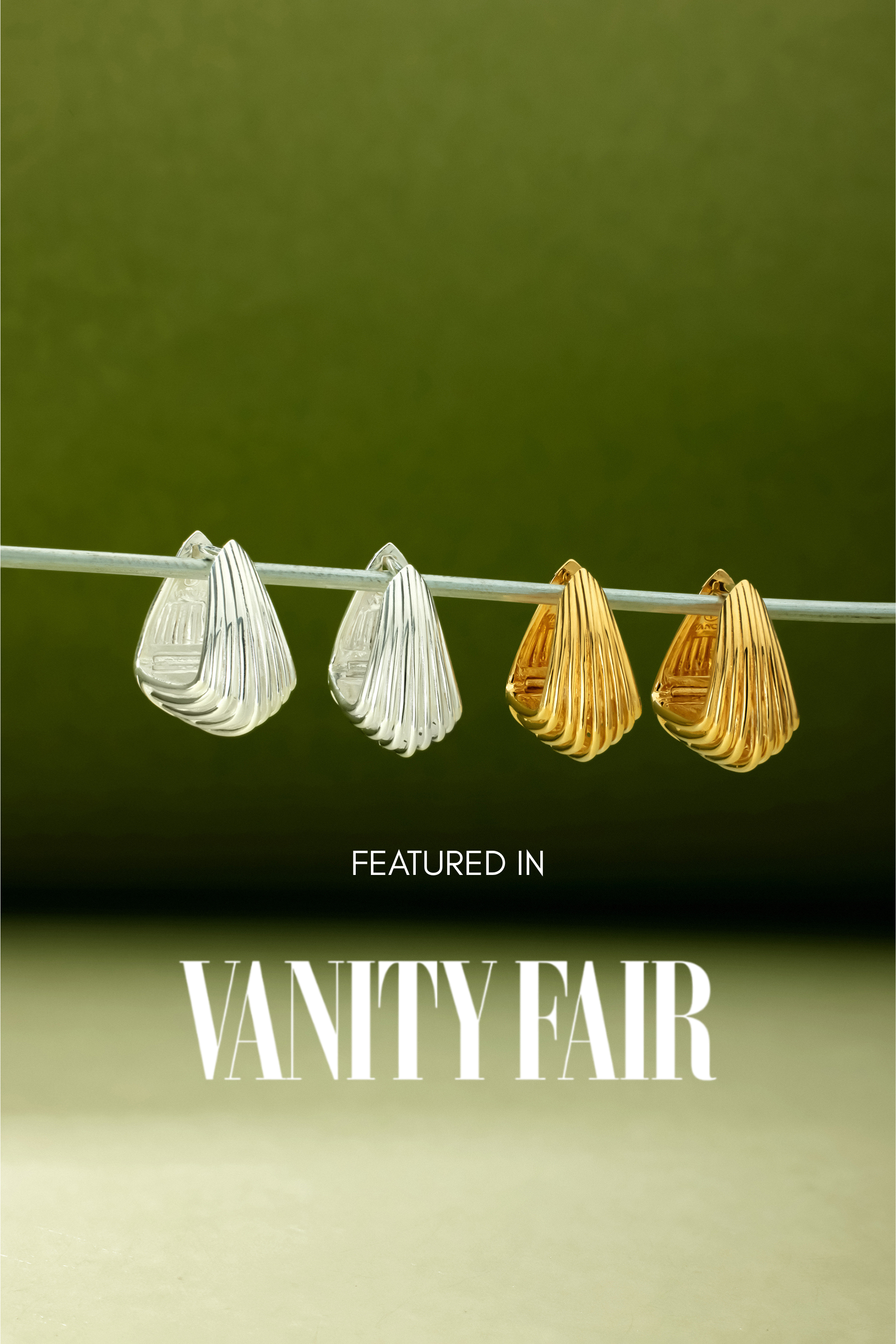 A pair of Juno Ridged Chunky Hoops in Silver hangs on a clear rod against a green gradient background. Text below reads, Featured in Vanity Fair.