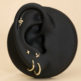 A black mannequin ear displays five gold earrings, including a 14K Solid Yellow Gold Snake Flat Back Stud at the top, alongside a small gold hoop, textured hoop, star stud, and bird earring, all set against a beige background.