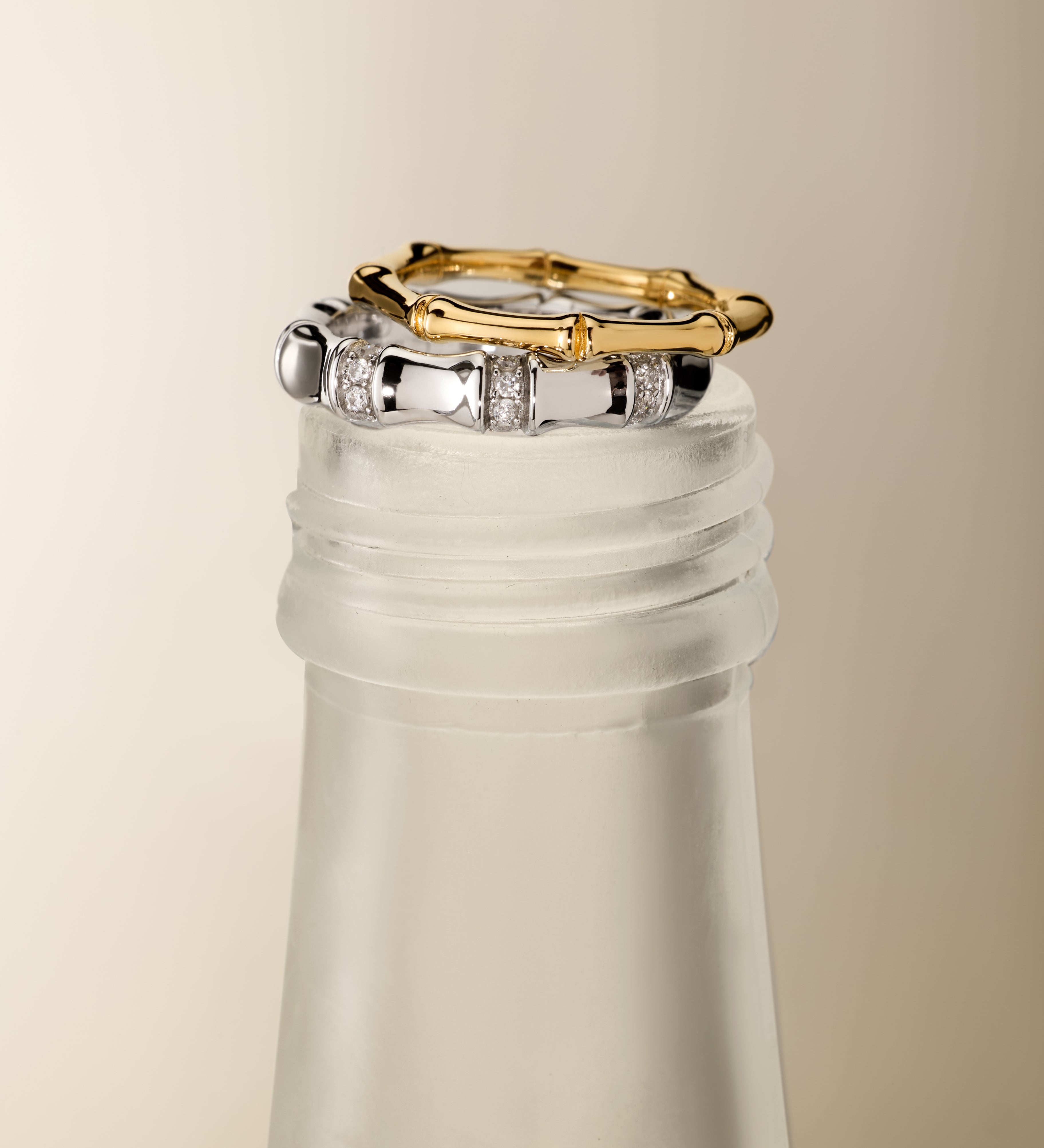 The Bamboo Chunky Crystal Ring in Silver is displayed stacked on the frosted neck of a glass bottle, set against a neutral beige background.