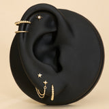 Gold earrings displayed on a black ear with a beige background